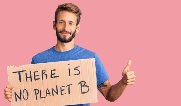Handsome blond man with beard holding there is no planet b banner smiling happy and positive, thumb up doing excellent and approval sign