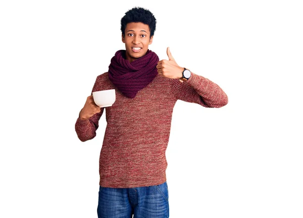 若いアフリカ系アメリカ人の男性は 冬のスカーフを着て ホットコーヒーのカップを飲んで笑顔幸せと正 親指アップ行う優れた承認サイン — ストック写真