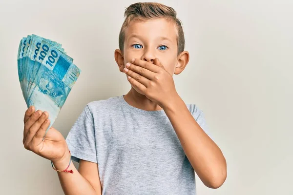 Urocze Kaukaskie Dziecko Trzymające 100 Brazylijskich Banknotów Zakrywających Usta Rękami — Zdjęcie stockowe