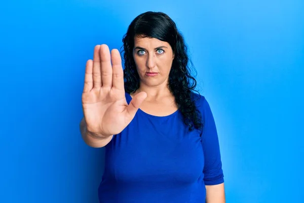 プラスサイズのブルネットの女性は手の手のひらで歌うのをやめるカジュアルな青いシャツを着ています 顔に負の重大なジェスチャーで — ストック写真