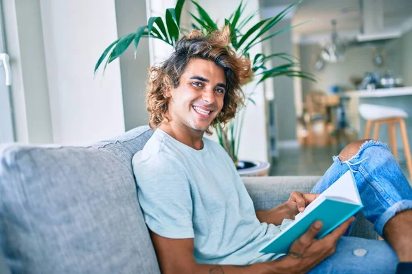 Joven Hispano Sonriendo Feliz Libro Lectura Casa —  Fotos de Stock