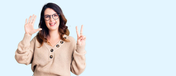 Красивая юная брюнетка в повседневной одежде и очках показывает и показывает пальцами номер семь, улыбаясь уверенно и счастливо. 