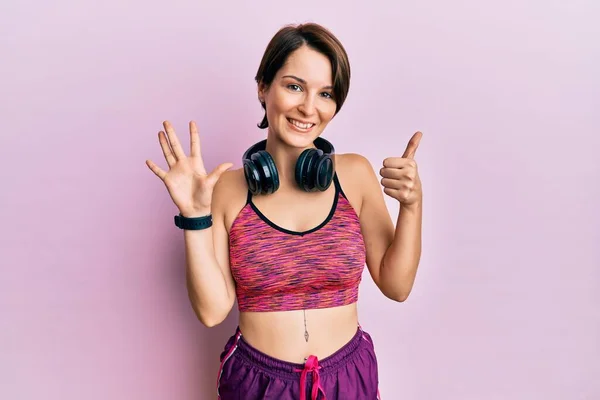 Młoda Brunetka Krótkimi Włosami Ubrana Odzież Sportową Słuchawki Pokazujące Wskazujące — Zdjęcie stockowe