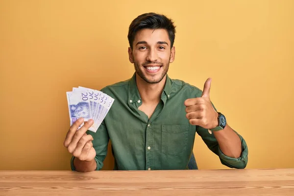 Joven Hombre Guapo Sosteniendo Billetes Coronas Suecas Sonriendo Feliz Positivo —  Fotos de Stock