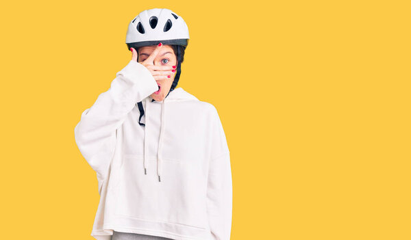 Beautiful brunette young woman wearing bike helmet and sporty clothes peeking in shock covering face and eyes with hand, looking through fingers with embarrassed expression. 