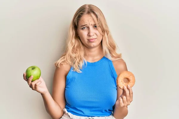 Jovencita Rubia Sosteniendo Manzana Verde Donut Expresión Despistada Confusa Concepto — Foto de Stock