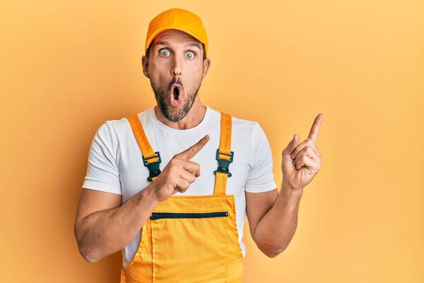 Young handsome man wearing handyman uniform pointing to the side afraid and shocked with surprise and amazed expression, fear and excited face. 