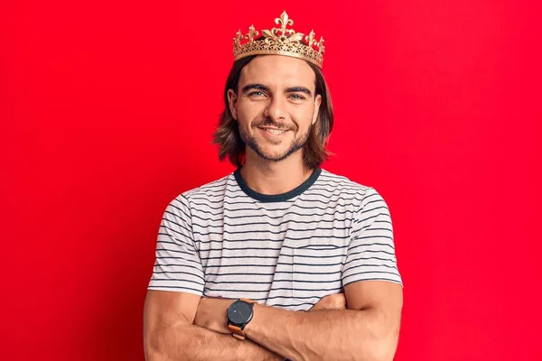 Young handsome man wearing prince crown happy face smiling with crossed arms looking at the camera. positive person.