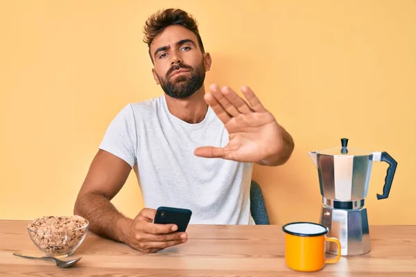 Joven Hispano Sentado Mesa Desayunando Usando Smartphone Con Mano Abierta — Foto de Stock