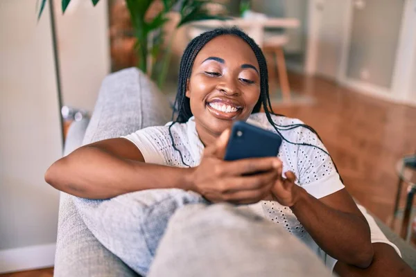 Joven Mujer Afroamericana Sonriendo Feliz Sentado Usando Teléfono Inteligente Casa —  Fotos de Stock
