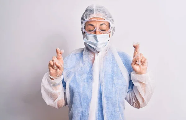 白い背景の上に保護コロナウイルス装置を身に着けている中年の看護師の女性ジェスチャー指は希望と目を閉じて笑顔を越えました 幸運と迷信の概念 — ストック写真