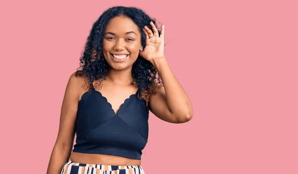 Young african american woman wearing casual clothes smiling with hand over ear listening an hearing to rumor or gossip. deafness concept.