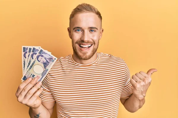 日本円の紙幣を持っている若い白人男性が口を開けて幸せそうに笑っている側を指差している — ストック写真