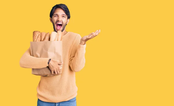 Bonito Homem Hispânico Segurando Saco Papel Com Pão Celebrando Vitória — Fotografia de Stock