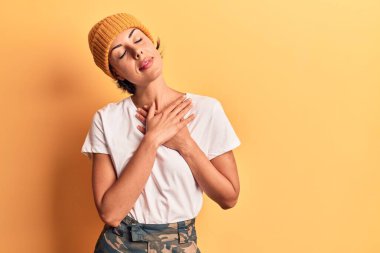 Yün şapka takan, elleri göğsünde, gözleri kapalı gülümseyen ve yüzünde minnet ifadesi olan genç ve güzel bir kadın. sağlık kavramı. 