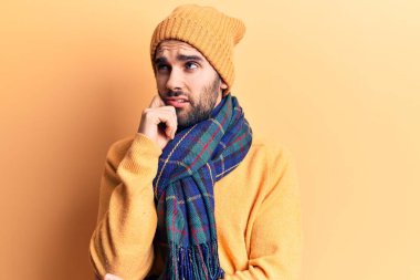 Sakallı, yün şapkalı ve eşarplı yakışıklı genç adam ciddi bir yüz ifadesiyle eli çenesinde soruyu düşünüyor, kafa karıştırıcı bir fikir. 