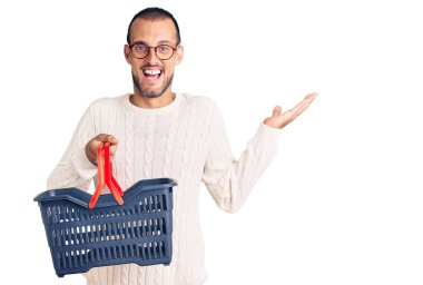Süpermarket alışveriş sepeti tutan genç yakışıklı adam zaferi mutlu bir gülümsemeyle ve kazanan yüz ifadesiyle kutluyor. 