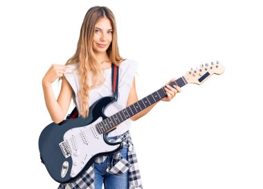 Güzel, beyaz, sarı saçlı, elektro gitar çalan mutlu ve gururlu bir kadını işaret eden bir kadın. 