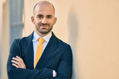 Genç, kel ve kollarını kavuşturmuş iş adamı şehirde mutlu bir şekilde gülümsüyor..