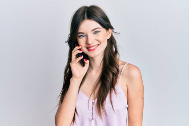 Genç, güzel, beyaz bir kız akıllı telefondan konuşuyor. Olumlu ve mutlu görünüyor. Kendine güvenen bir gülümsemeyle dişlerini gösteriyor. 