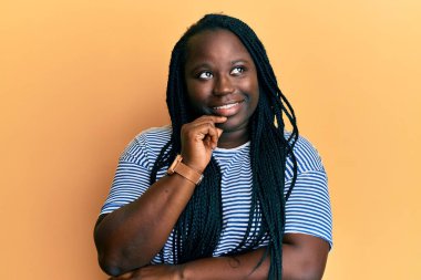 Saçları örgülü, sıradan kıyafetler giyen genç siyahi bir kadın kameraya kollarını kavuşturup çenesi üzerinde kendinden emin bir şekilde bakıyor. Olumlu düşünmek. 