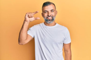 Orta yaşlı, beyaz tişört giyen, gülümseyen, kendine güvenen, el hareketi yapan, parmaklarıyla işaret yapan ve kameraya bakan yakışıklı bir adam. ölçüm kavramı. 