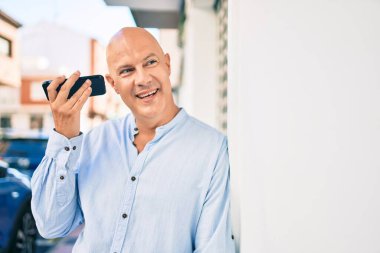 Orta yaşlı kel adam gülümsüyor. Şehirdeki akıllı telefonu kullanarak mutlu bir sesli mesaj dinliyor..