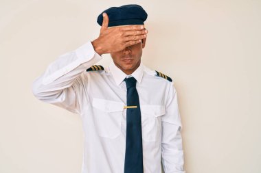 Uçak pilotu üniforması giyen genç İspanyol adam, gözlerini eliyle kapatıyor, ciddi ve üzgün görünüyor. Görme, saklama ve reddetme konsepti 