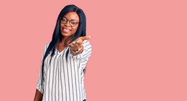 Genç Afrikalı Amerikalı kadın günlük kıyafetler ve gözlük takıyor. Gülümsüyor. Avuç içi dolusu yardım eli uzatıyor ve kabul ediyor.. 