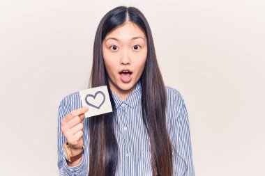 Genç, güzel Çinli bir kadın elinde kalp şeklinde bir hatıra tutuyor. Şaşırtmak için ağzı açık ve korkmuş. İnançsız bir yüz. 