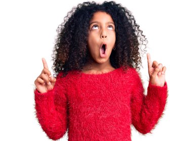 Kış süveteri giyen kıvırcık saçlı Afro-Amerikalı çocuk şaşırdı ve şaşırdı. Parmaklarıyla işaret etti ve kollarını kaldırdı.. 