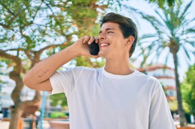 Genç beyaz adam gülümsüyor. Şehirdeki akıllı telefondan konuşuyor..