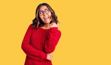 Kırmızı süveter giyen, mutlu yüzlü gülümseyen ve baş parmağıyla yan tarafı gösteren güzel, melez bir kadın.. 