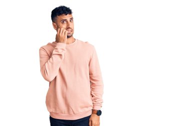 Günlük kıyafetler giyen genç İspanyol adam gergin ve gergin görünüyor. Ağzı tırnak yiyen eller. anksiyete. 