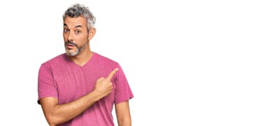 Orta yaşlı, gri saçlı, günlük giysiler giyen, el parmaklarıyla işaret eden, ciddi ve sakin bir yüz ifadesi olan bir adam. 