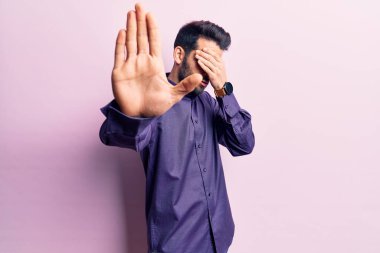 Sakallı, sıradan tişörtlü, elleriyle gözlerini kapatan, üzgün ve korku dolu hareketler yapan genç yakışıklı bir adam. utangaç ve olumsuz kavram. 