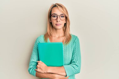 Güzel sarışın kadın kitap tutuyor, gözlük takıyor ve yüzünde ciddi bir ifade var. Basit ve doğal bir şekilde kameraya bakıyorsun.. 