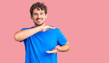 Kıvırcık saçlı, sıradan kıyafetler giyen, elleri büyük ve büyük boy işareti gösteren genç yakışıklı bir adam. Ölçü sembolü. Kameraya bakıp gülümsüyor. ölçüm kavramı. 