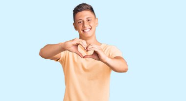 Gündelik kıyafetler giyen, aşık gülümseyen ve elleriyle kalp sembolü çizen genç yakışıklı bir adam. romantik kavram. 