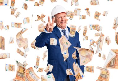 Kıdemli yakışıklı, gri saçlı, takım elbiseli, mimar şapkalı, iki numaralı parmaklarıyla iki numarayı gösteren, kendinden emin ve mutlu bir şekilde gülümseyen adam..