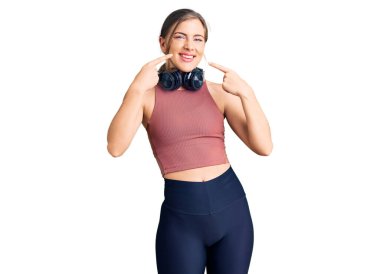 Güzel, beyaz, spor kıyafetleri giyen, kulaklık takan, gülümseyen, parmaklarıyla dişlerini ve ağzını gösteren bir kadın. diş sağlığı kavramı. 