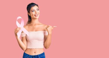 Kanser farkındalığı taşıyan genç ve güzel bir kadın. Pembe kurdele başparmağını yana uzatmış, ağzı açık gülümsüyor. 