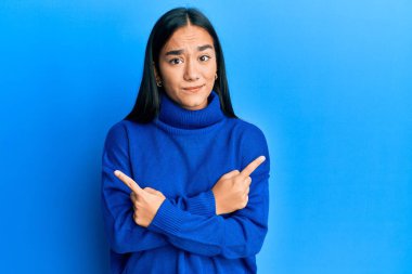 Günlük kışlık süveter giyen genç Asyalı kadın parmaklarıyla her iki tarafı işaret ediyor, farklı yönlere bakıyor. 