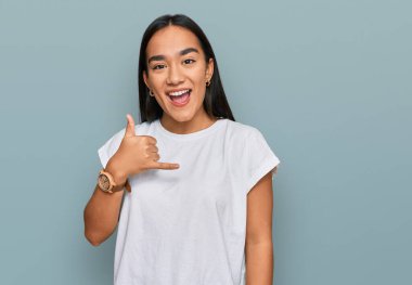 Genç Asyalı kadın, günlük beyaz tişört giyip gülümsüyor telefonla el ve parmaklarıyla jest yapıyor telefonda konuşuyor gibi. iletişim kavramları. 