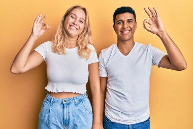Beyaz tişört giyen, olumlu gülümseyen genç bir çift el ve parmaklarıyla 