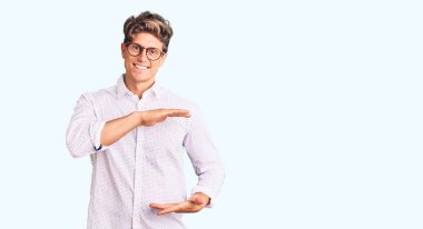 İş kıyafetleri ve gözlük takan genç yakışıklı adam büyük ve büyük boyut işareti gösteren el hareketleriyle işaret ediyor. Kameraya bakıp gülümsüyor. ölçüm kavramı. 