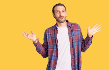 Sıradan kıyafetler giyen, elleri ve kolları havada, kafası karışmış genç ve yakışıklı bir adam. şüphe kavramı. 