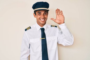 İspanyol pilot üniforması giyen genç adam merhaba diyor mutlu ve gülümseyen, dostça bir hoş geldin jesti 