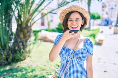 Genç, güzel bir kız mutlu bir şekilde gülümsüyor. Akıllı telefon kullanarak şehrin caddesinde yürüyor.