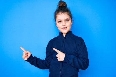 Hoş İspanyol çocuk günlük kıyafetler giyiyor gülümsüyor ve kameraya bakıyor iki eliyle ve parmaklarıyla kenarı işaret ediyor.. 